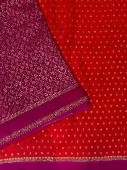 A vibrant red Banarasi saree with all-over buttas, paired with a contrasting purple brocade blouse piece. This is a classic, "classy" combination that is perfect for celebrations.