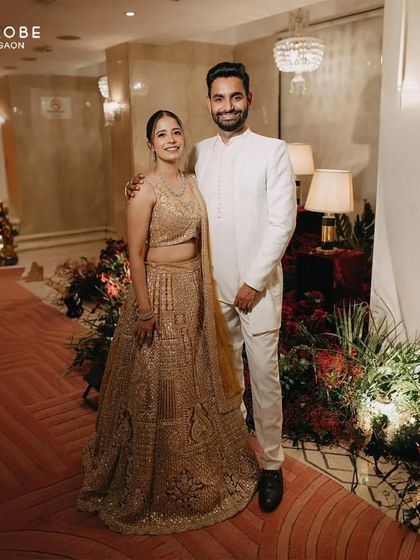A full-length shot of the couple, showcasing his all-white sherwani and her golden lehenga. Coordinated outfits like these make for beautiful pre-wedding pictures.