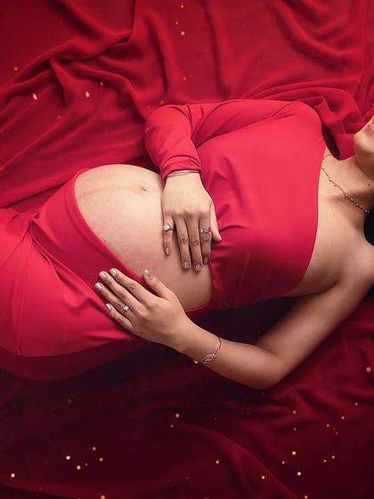 A moment of pure bliss. This artistic top-down shot on a bed of red fabric captures the serene joy of pregnancy. The scattered gold glitter adds a touch of magic.