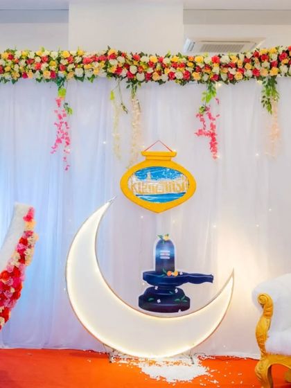 A close-up of the backdrop for a naming ceremony, featuring a lighted moon prop with a Shivling, blending spiritual elements with modern decor for a unique theme.