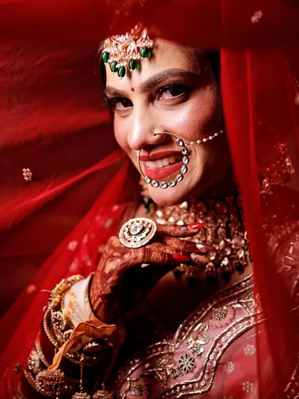 A vibrant close-up of a bride smiling from behind her red veil, her eyes full of happiness.