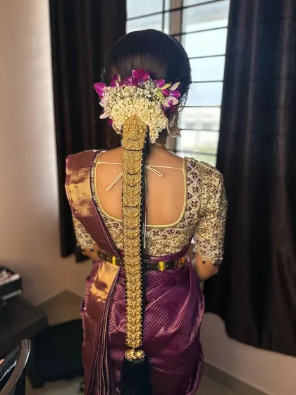 This Muhurtham braid is decorated with a full set of gold temple jewellery and a mix of jasmine and purple flowers. The combination creates a rich and regal bridal hairstyle.