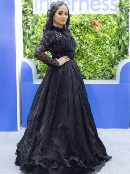 A full-length shot of a stunning black gown. The sheer, embroidered high-neck top and the voluminous layered skirt create a dramatic and glamorous look for any formal event.