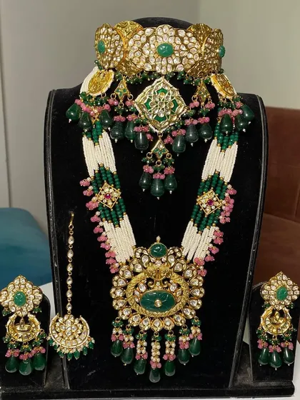 This royal bridal set combines a wide Kundan choker with a long, elegant rani haar. The green beads and white pearls make it a versatile rental option for pairing with many different lehenga colors.