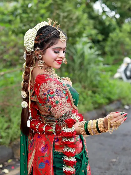 A happy bride in a green and red saree, adorned with fresh rose garlands on her arms, adding a unique and fragrant touch to her look.