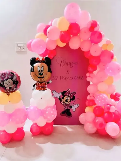 A sweet Minnie Mouse "1/2 Way to One" celebration. This decoration features a pink arched backdrop, balloon columns topped with Minnie Mouse foils, and a colorful balloon arch.