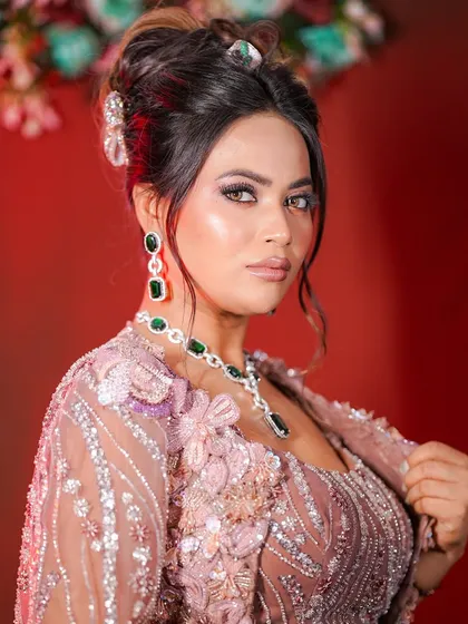 A full view of the elegant party look. The dusty pink, heavily embellished outfit is paired with a chic updo and statement emerald jewelry.