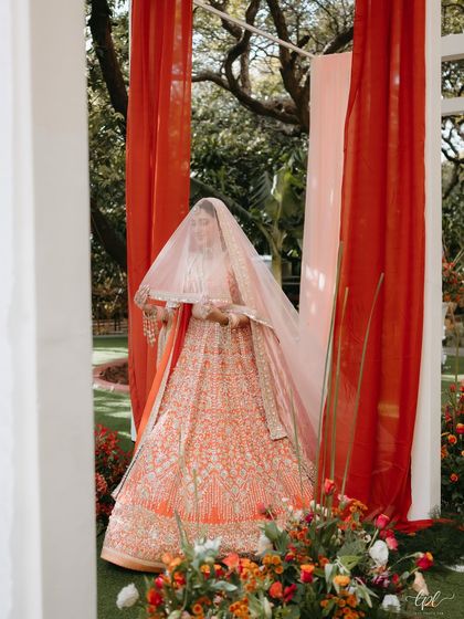 The bride's entrance is a moment of pure magic. Here, she walks through an entryway of flowing white and coral drapes, perfectly complementing her beautiful lehenga.