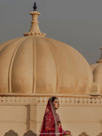 A regal bridal portrait with the iconic domes of The Oberoi Udaivilas creating a majestic backdrop against the evening sky.