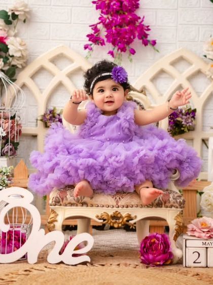 A royal first birthday. This little princess, surrounded by lavender and pink flowers, looks absolutely regal on her mini throne. The 'One' sign marks the special occasion.