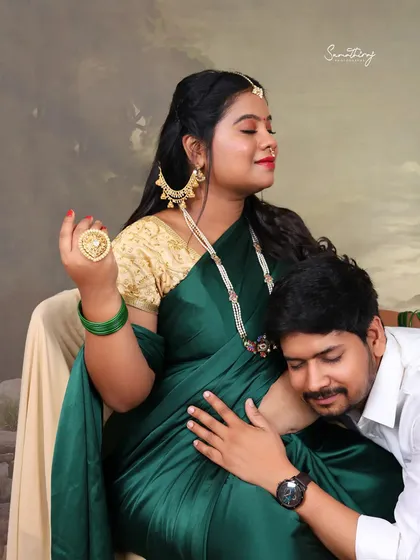 A candid and intimate moment where the father-to-be listens to the baby bump. The rich green saree and traditional jewelry add a touch of elegance to this heartwarming shot.