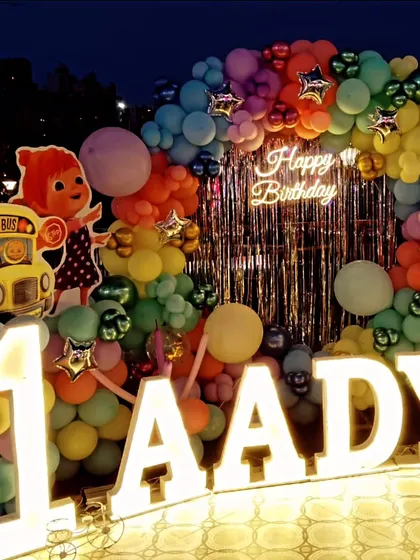 A vibrant Cocomelon birthday setup with a multi-colored balloon arch, silver fringe curtain, and large marquee letters spelling the name 'AADYA'.