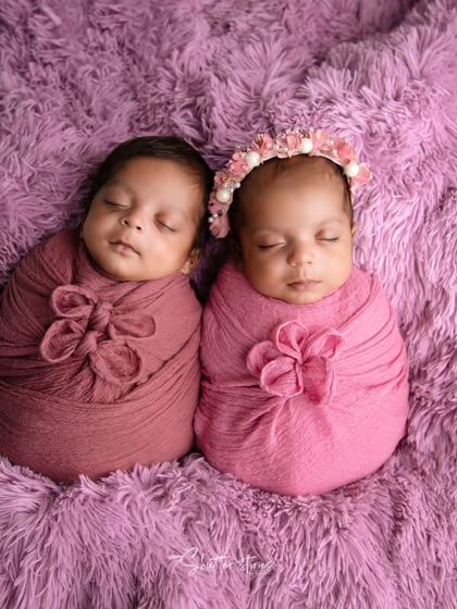 A beautiful portrait of twin babies nestled together on a soft purple rug. Coordinating wraps with different floral knot styles adds individuality while maintaining a cohesive look.