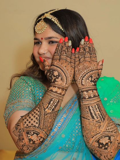 A happy bride showcasing her full bridal mehendi. The design features a mix of traditional Indian motifs, including floral patterns and detailed finger work.
