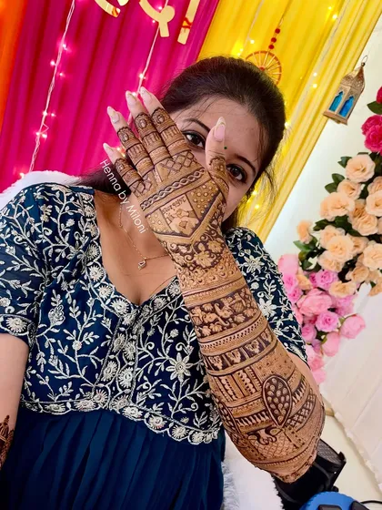 A happy bride showing off her full-arm mehendi. The design is a mix of traditional Indian motifs, creating a dense and beautiful pattern perfect for her wedding day.