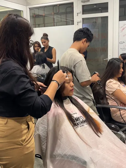 A student practices a haircut on a live model, with a trainer providing guidance and support.