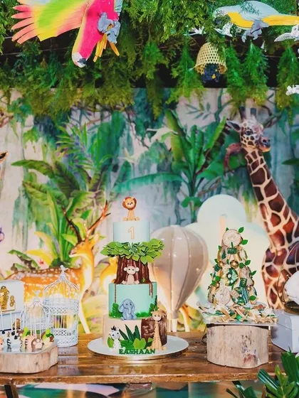 A magical cake table setup for Eshaan's jungle party. The table is surrounded by dense greenery, animal figures, and a custom jungle-themed cake, all under a canopy of hanging decorations.