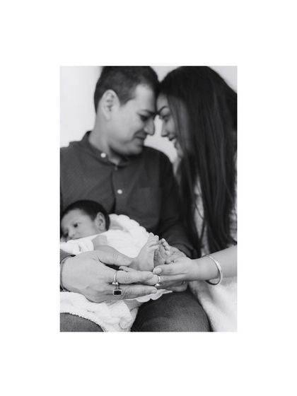 A black and white portrait of a family holding their newborn's tiny feet. A creative and emotional shot that focuses on the details.