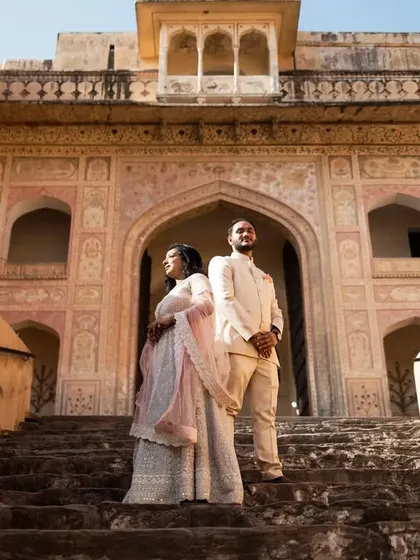 A powerful, statuesque pose on the steps of a Jaipur fort. The couple stands together, looking out towards their future, framed by the grandeur of the ancient stone architecture.