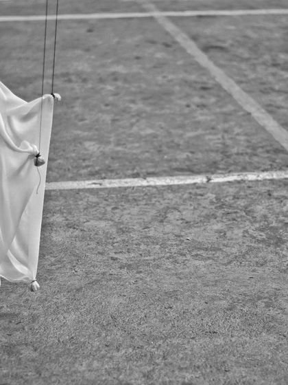 A single, simple marionette made of white cloth stands on the ground. This artistic, black and white shot highlights the elegant simplicity of handmade puppets.