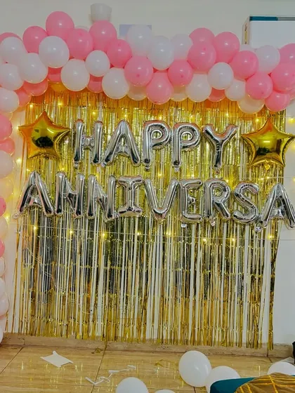 A classic anniversary backdrop with a pink and white balloon arch, a gold tinsel curtain, and 'Happy Anniversary' foil letters.