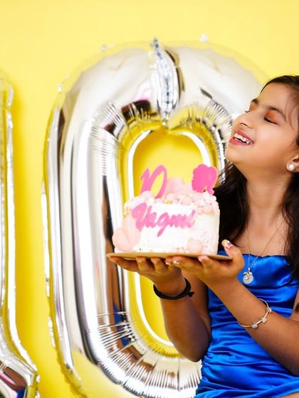 Celebrating double digits! A young girl smiles as she holds her 10th birthday cake, with giant silver '10' balloons in the background.