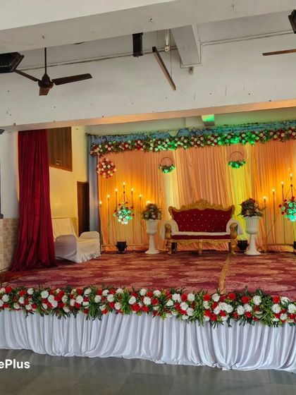 A stage decoration with a peach and red color scheme. The floral arrangements along the top and front of the stage, paired with a red velvet sofa, create a warm and inviting look.