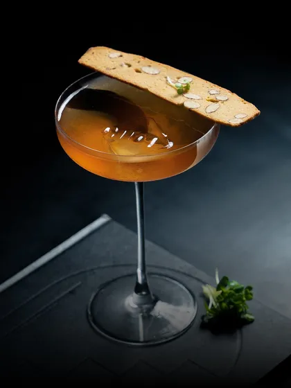 This is our 'Nilgiri' cocktail, a unique blend of smokey whiskey, coffee, eucalyptus, lavender milk, and vermouth, served with an almond biscotti.