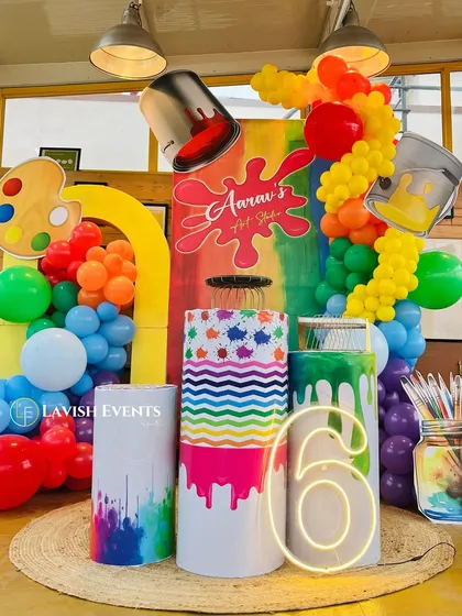 A close-up of the vibrant art studio party decor, showing the custom-printed pedestals with paint drip effects and a neon number '6'.