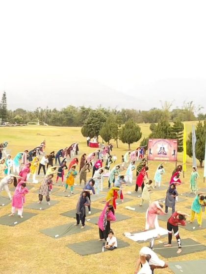 A view of a diverse group of participants, including women in colorful traditional attire, enjoying a morning of yoga in the open field.