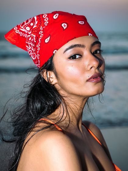 A close-up from the same beach series, this time with the bandana worn on the head. The model's direct gaze and the clean background of the sea and sky make this a striking and engaging portrait.