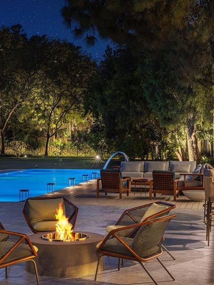 The outdoor lounge area at night, with the pool and landscape lighting creating a magical ambiance. The fire pit provides a warm gathering spot for cool evenings.