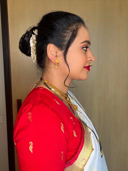 A side profile showing the elegant hair updo for this Nauvari saree look. The neat bun is accented with a gold accessory and soft tendrils to frame the face.