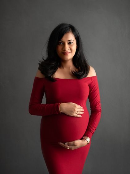 A bold and beautiful choice. This mom-to-be looks absolutely stunning in a classic, off-the-shoulder red gown against a simple grey backdrop.