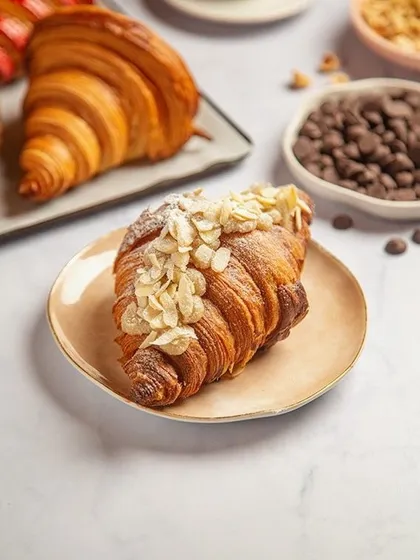 The beauty of a perfect croissant is in its flaky layers. We styled this shot with a clean, bright background and scattered almonds and chocolate chips to suggest its ingredients and create a fresh, bakery-like feel.