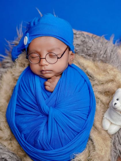 A tiny scholar dreaming of big books. The combination of the blue swaddle, fluffy nest, and little round glasses makes for a truly unique and adorable portrait.