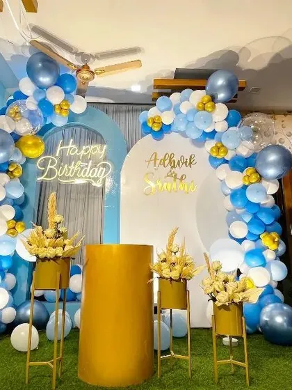 A double-arch backdrop in shades of blue and white for a birthday party, personalized with names and a neon sign.