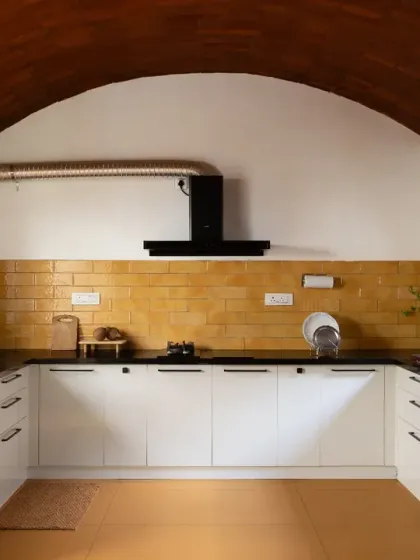 The open kitchen in the Basavanagudi house features a stunning vaulted ceiling made of brick and a backsplash of handmade yellow tiles. It's a bright, cheerful, and highly functional space that opens into the dining area.