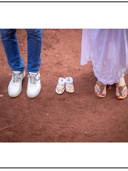 A creative shot focusing on the feet of the parents-to-be next to a tiny pair of baby shoes, symbolizing the new member joining their family.
