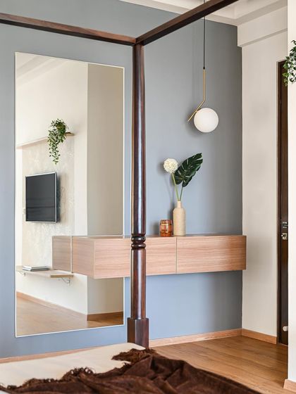 A chic dresser area in the master bedroom. A large mirror visually expands the space, while the floating wooden console provides storage without taking up floor space. The reflection shows the TV unit on the opposite wall.