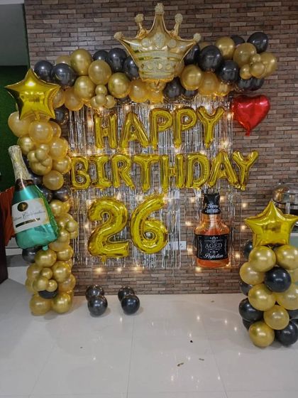 A fun 26th birthday setup for adults, featuring black and gold balloons, a foil curtain, and large champagne and whiskey bottle foil balloons.
