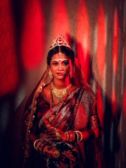 A dramatic portrait of the Bengali bride in her traditional attire. The red lighting creates a powerful and artistic image, highlighting her beauty.