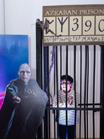 An Azkaban Prison photo booth, where a young guest playfully poses behind bars next to a menacing Voldemort cutout.