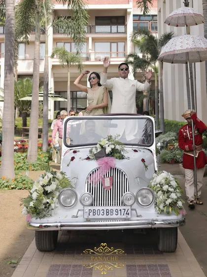 The groom's baraat arrives in style in a vintage white car, adorned with fresh flowers.