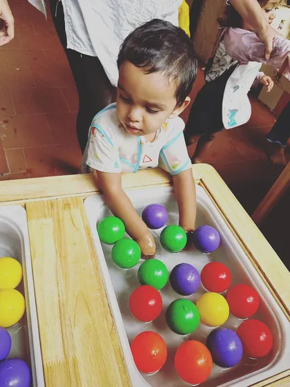 A toddler fully engaged in sensory water play. He is carefully exploring the colorful balls floating in the water table, an activity that helps develop hand-eye coordination and tactile awareness.
