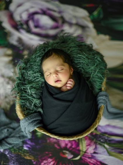 An overhead view of the baby in a black wrap, set against a dramatic purple floral backdrop for an artistic and rich composition.