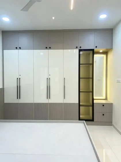 A full view of a modern wardrobe unit with a built-in dressing corner. The design combines high-gloss white and grey fluted panels, with a backlit mirror and a glass display cabinet for a touch of elegance.