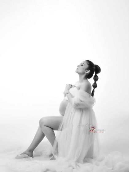 A graceful black and white portrait of an expectant mother seated on a cloud-like surface. The simple styling and her peaceful expression create a timeless and artistic image.
