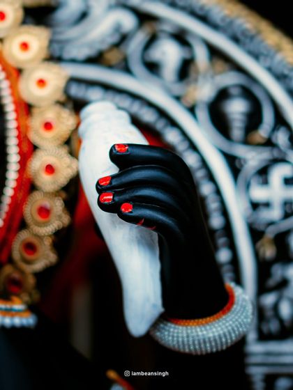 Another detailed shot of the idol's hand, this time holding the sacred conch. The contrast of the black hand, red nails, and white conch makes for a visually striking composition.
