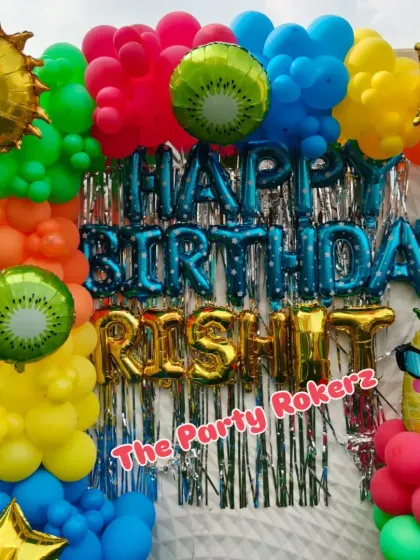 A vibrant Pool Party theme for a terrace celebration. The decor features a bright, multi-colored balloon arch, a shimmer backdrop, and fun foil balloons like a smiling sun, kiwi, and pineapple.